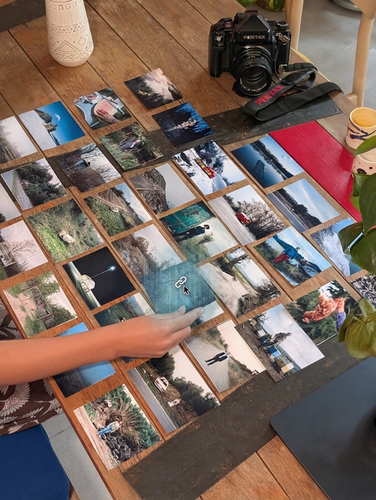 Prints laid out in a grid across a table, a hand reaching in to move one
